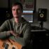 a man with a guitar on a background of music equipment